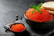 Red caviar served in a bowl and caviar sandwiches on a black stone board against a dark backdrop