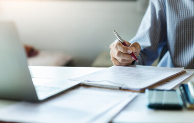 Wall Mural - Asian businessman reviewing document reports at office workplace with computer laptop. legal expert, professional lawyer reading and checking financial documents or insurance contract before sign