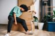 © Queenmoonlite Studio - Asian man sitting near pile of cardboard boxes tired after moving house