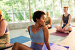 © Flamingo Images - A beautiful black woman sits on a mat with her friends in yoga class