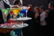waiter serving tray of colorful martinis to guests at an upscale event