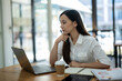 © Wasana - A thoughtful young professional woman concentrates while working on her laptop in a modern office setting..