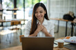 © Wasana - Content Asian businesswoman smiling and feeling grateful during a pleasant conversation over a laptop in a sunny office..