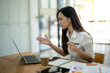 © Wasana - An engaged Asian businesswoman gestures while explaining a concept during a video conference on her laptop in the office..