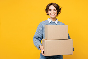 Wall Mural - Young smiling happy cheerful woman she wears grey knitted sweater shirt casual clothes hold cardboard boxes looking camera isolated on plain yellow color background studio portrait. Lifestyle concept.