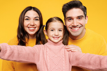 Wall Mural - Close up young fun happy parents mom dad with child kid girl 7-8 years old wearing pink sweater casual clothes do selfie shot mobile cell phone isolated on plain yellow background. Family day concept.