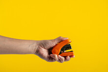 Orange Stapler In Hand Isolated On Yellow Background
