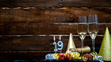 Solemn Background For The Anniversary With The Number  19. Happy Birthday Background On Brown Wooden Background With Champagne Bottle And Champagne Glasses. Beautiful Holiday Decorations Copy Space.