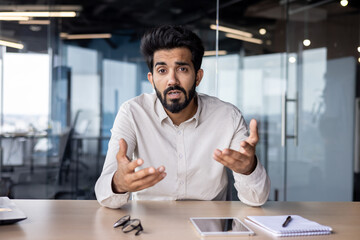 Wall Mural - Close-up photo of a young Indian male businessman, an office worker who communicates with clients via video call, conducts business training, online conference in the office in front of the camera