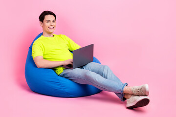 Sticker - Full length photo of cheerful cool man dressed yellow t-shirt sitting bean bag chatting device empty space isolated pink color background