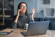 Happy business woman talking on cell phone sitting at table and working. Asian female sitting at office having telephonic conversation with client and smiling with look away
