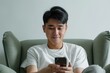 © Wanderson-oliveira - Handsome young Asian guy using cellphone, sitting on a sofa