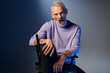 © LIGHTFIELD STUDIOS - stylish mature man in purple sweatshirt sitting on chair while grimacing and looking at camera