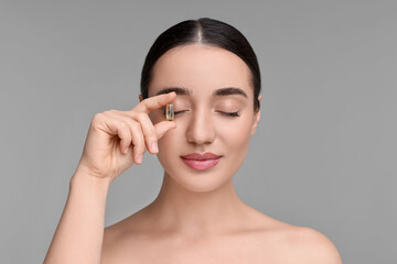 Poster - Beautiful young woman with vitamin pill on grey background