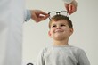 Vision testing. Ophthalmologist giving glasses to little boy indoors, low angle view