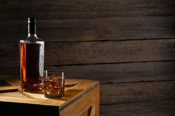 Wall Mural - Whiskey with ice cubes in glass and bottle on wooden crate, space for text