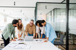 © Vadim Pastuh - Diverse team huddles around table, and looks at a laptop screen in a bright office, closely reviewing documents and digital content together, showcasing a moment of collective focus and determination