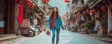 Fototapeta Uliczki - A joyful young Asian Chinese woman crosses the road while carrying a skateboard in an old town, radiating a sense of happiness and urban vibrancy.