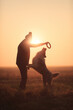 silhouette of an australian shepherd dog sitting jumping for a toy with a woman against a setting sun
