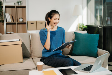 Asian Business woman Talking on the phone and using a laptop with a smile while sitting on sofa