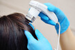 A close-up of a cosmetologist-trichologist diagnoses the condition of the patient's hair using a trichoscope.