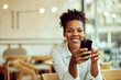 Portrait of a smiling African woman, using a mobile phone, sitting at the cafe, alone.