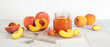 Fresh peaches and sweet jam in jar on table against white background