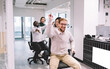© BullRun - Cheerful multiethnic employees rolling colleagues on chairs