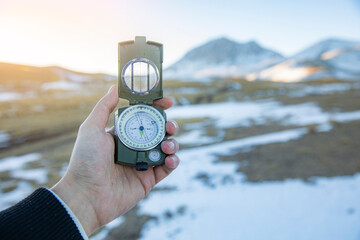 Wall Mural - hand holding compass in winter mountains background