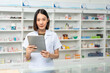 © Chanakon - Beautiful asian woman pharmacist checks inventory of medicine in pharmacy drugstore. Professional Female Pharmacist wearing uniform standing near drugs shelves working with tablet.