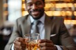 A well-dressed man enjoys a refreshing pint of beer, his smile reflecting the joy of a drink shared among friends in a cozy indoor bar