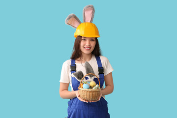 Poster - Female Asian worker in bunny ears with Easter eggs on blue background