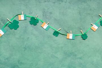 Paper garland with clover and Irish flags for St. Patrick's Day celebration on green background