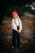 A little blonde girl in a red beret and suspenders with a book in nature