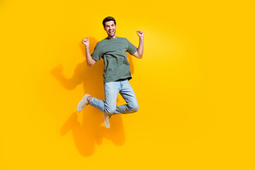 Poster - Full length photo of excited lucky guy wear khaki t-shirt jumping high rising fists empty space isolated yellow color background