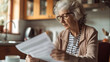 Elderly woman holds a paper bill as she endeavors to decipher its contents, managing her finances. Vintage and blurry kitchen background.
