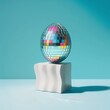 Easter disco ball egg standing by white pedestal on a blue pastel background. Abstract, minimal Easter concept.