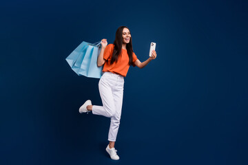 Poster - Full length photo of positive funky woman dressed orange t-shirt rising shoppers vlogging modern gadget isolated dark blue color background