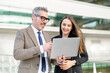 © Vadim Pastuh - A senior businessman and a younger female colleague engage with content on a laptop together outdoors, representing mentorship and collaboration in a modern business environment