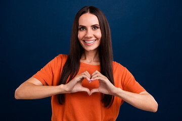 Sticker - Photo of good mood kind woman with straight hairdo dressed orange t-shirt fingers showing heart symbol isolated on dark blue background