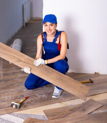 Wall Mural - Female worker in blue construction overalls and cap installing new wooden laminate flooring sitting squat. Home renovation concept