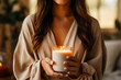 A woman holding a candle in a glass container, cozy autumn style, neutral colors.