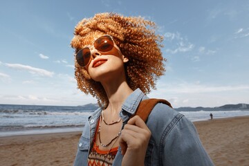 Wall Mural - Joyful Journey: Smiling Woman on a Beach with Curly Hair and Backpack, Enjoying the Freedom and Beauty of Nature