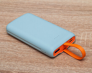 A modern gadget for charging devices, a power bank with an orange USB handle on a wooden background.