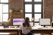 © Wavebreak Media - Young Caucasian woman works at a dual-monitor desk setup in a casual business office