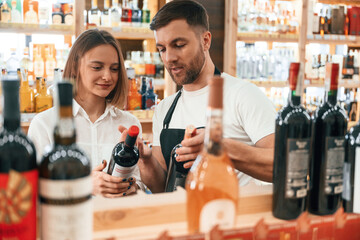 Wall Mural - Customer service. The shop owner helps a young woman to choose a good wine