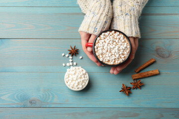 Sticker - Woman with cup of tasty hot chocolate and marshmallows at light blue wooden table, top view. Space for text