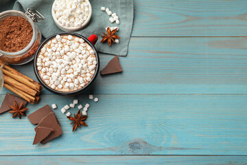 Wall Mural - Tasty hot chocolate with marshmallows and ingredients on light blue wooden table, flat lay. Space for text