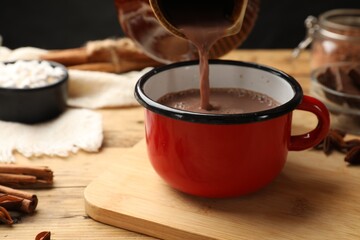 Wall Mural - Pouring tasty hot chocolate into cup at wooden table, closeup