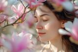 Fototapeta  - A beautiful young woman standing against a backdrop of delicate spring magnolia flowers